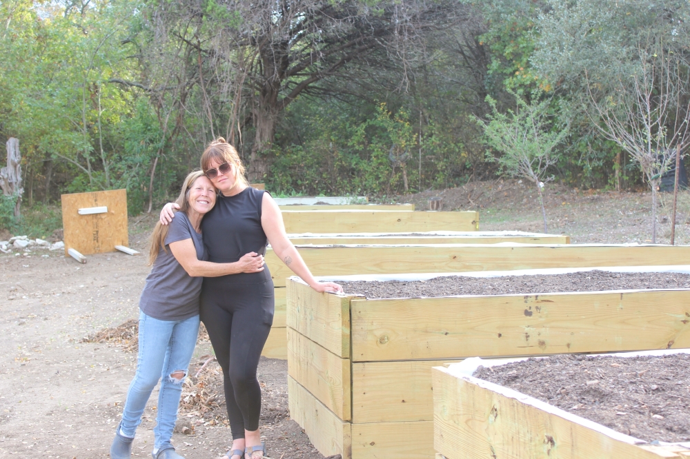 From left, Brandy Gerstner stands with her daughter Ashlee Willis beside the new planter boxes they rebuilt months after catastrophic July flooding destroyed their homes and seasoning business. (Haley McLeod/Community Impact)