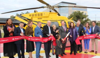 People cut a ribbon at a celebratory event standing in front of a helicopter