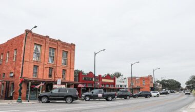 A large red brick building next to more businesses on a street in downtown Buda.