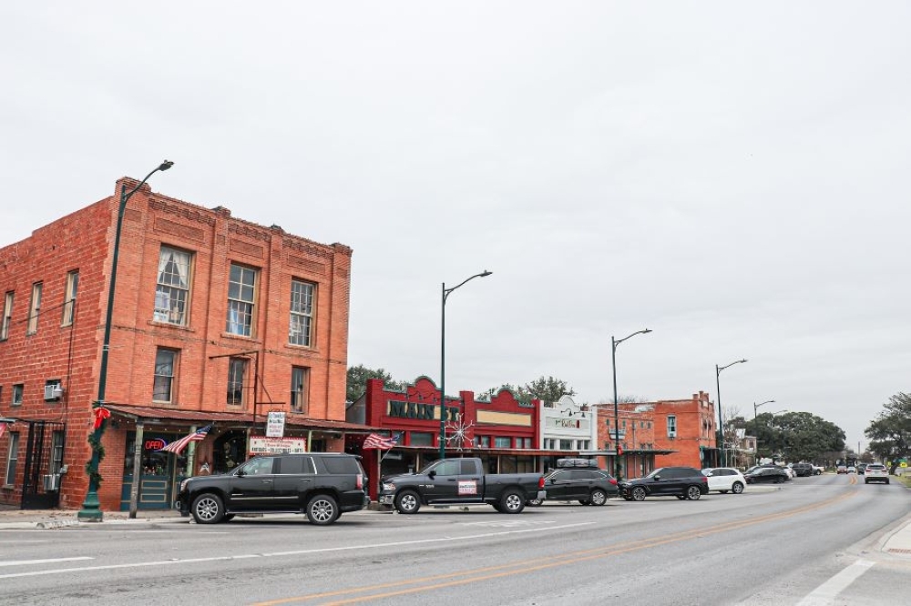 A large red brick building next to more businesses on a street in downtown Buda.