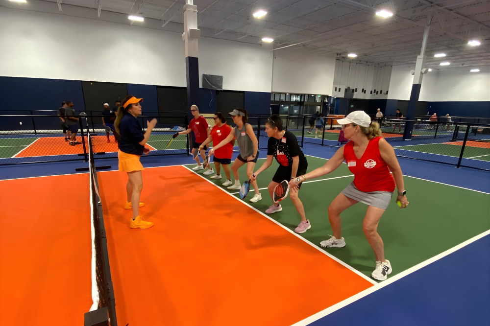 Pickleball enthusiasts playing on state-of-the-art indoor courts at Dill Dinkers Plano, featuring CushionX flooring for reduced joint strain, a climate-controlled environment, and expert coaching for beginners to competitive players.