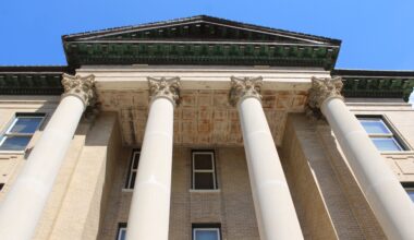 The Hays County courthouse, four large white pillars lead to the green, triangular roof.
