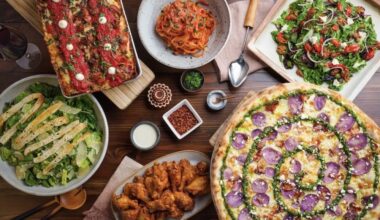 several pizzas, salads, pasta and wings on a table