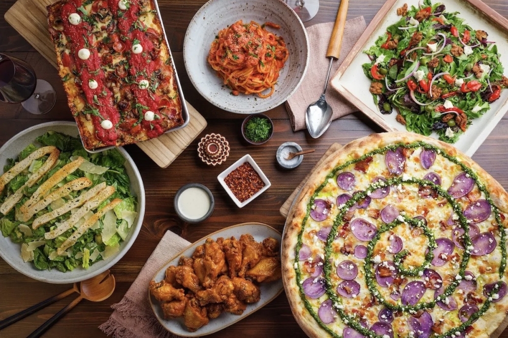 several pizzas, salads, pasta and wings on a table