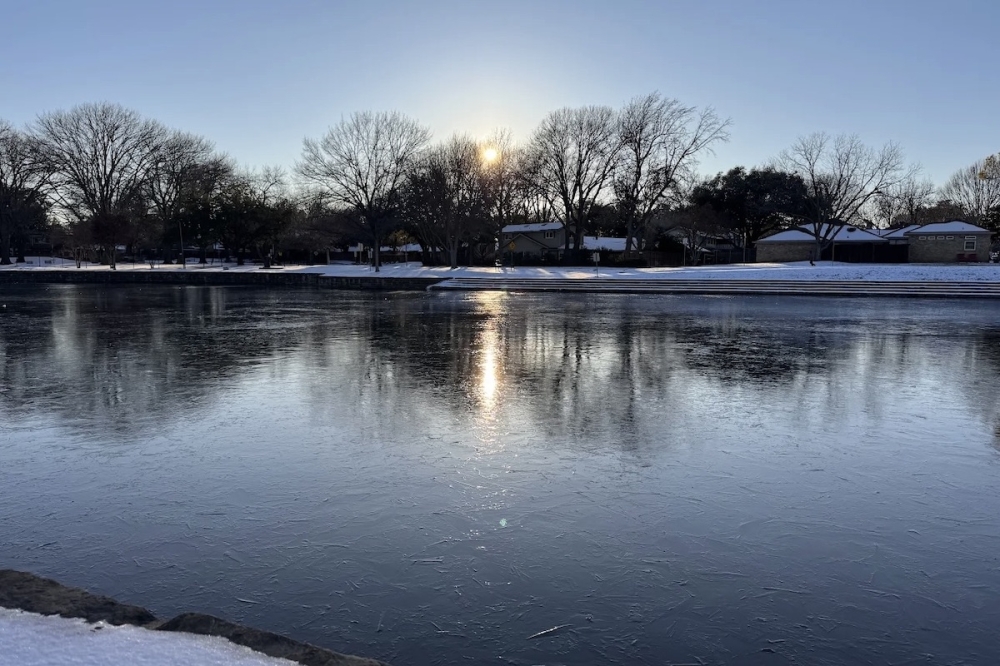 a large park lake with a thin layer of ice on the top