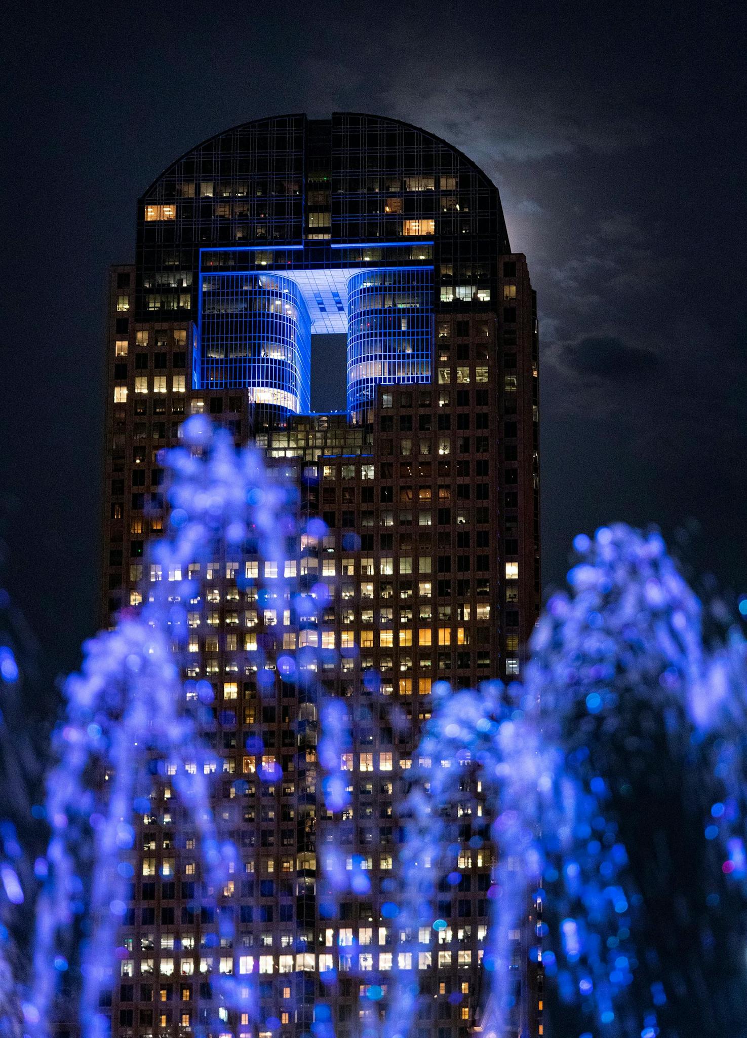 May 10 9:02 P.M. The moon glows behind Chase Tower as water from the Nancy Best Fountain at Klyde Warren Park arcs in the foreground.
