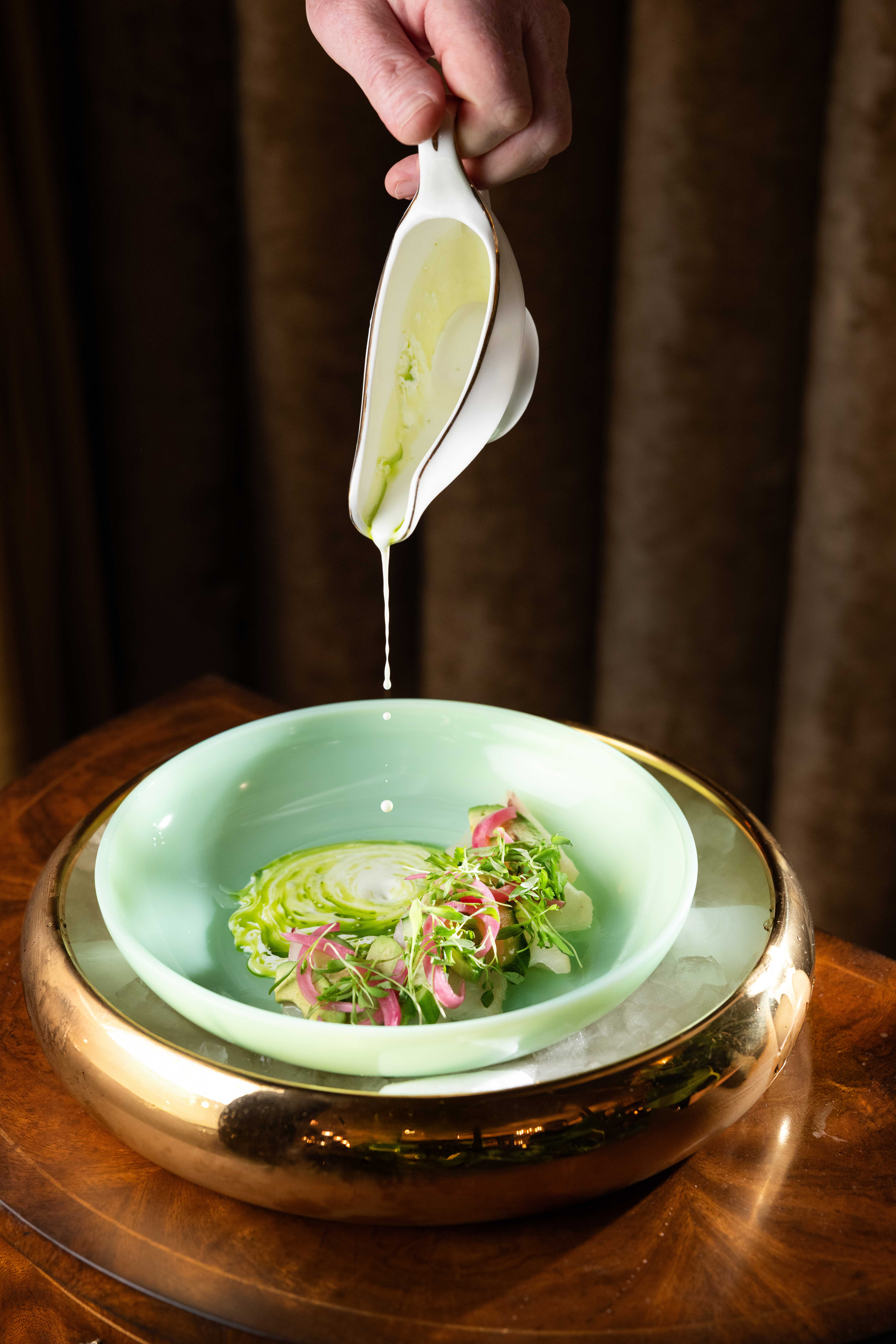 Hand pouring green sauce onto a decorative dish.
