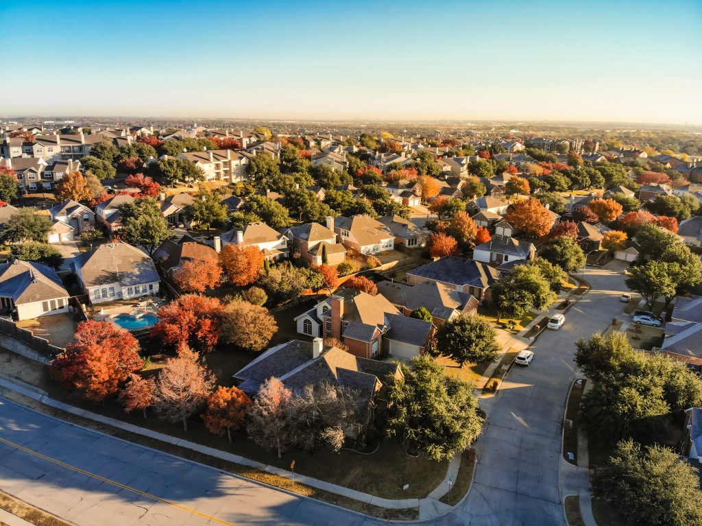 Top-down aerial view of a Dallas, Texas suburb in autumn with colorful foliage.