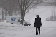Malik Jones walks along a snow-covered street with a U.S. Postal Service truck in the...