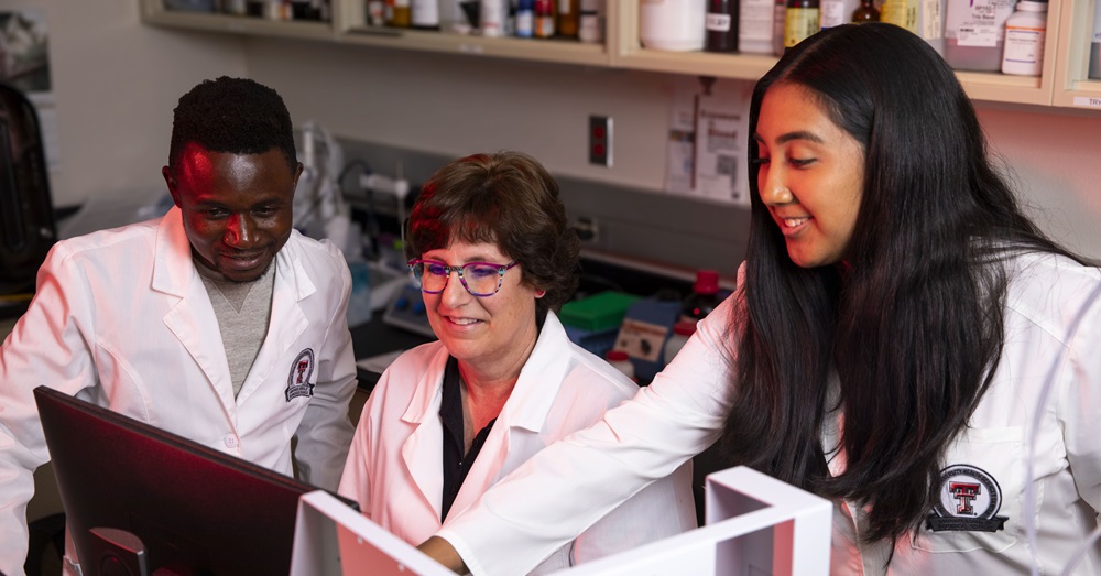 three biotechnology experts in lab coats look at a screen