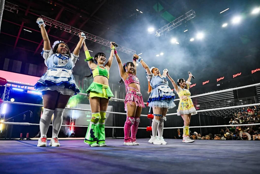 Image shows a group of TJPW wrestlers holding their arms up together in costume inside a ring.