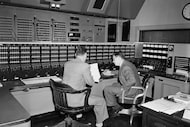 Two employees huddle in the Voice of America's radio control room in New York, Feb. 27,...
