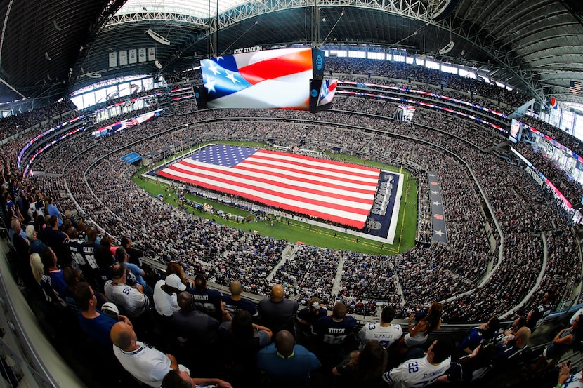 Representatives from the branches of police, fire and military stretch a field-sized U.S....