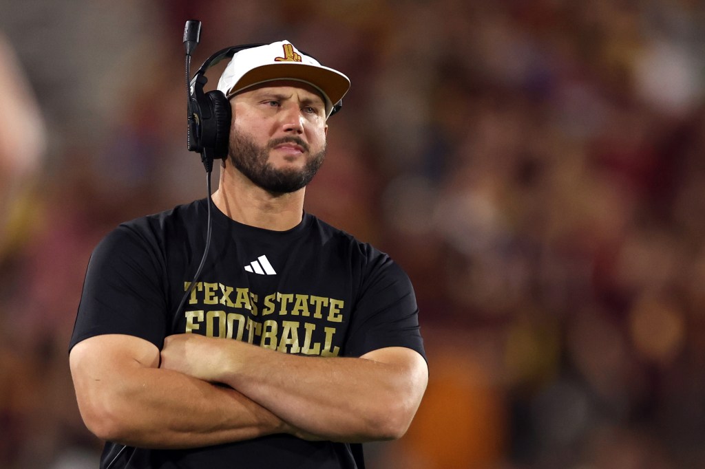 A football coach wearing a Texas State Football shirt and a hat, with a headset on.