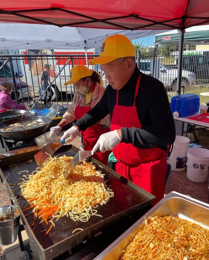 Image shows two vendors at the Otaku Food Festival preparing a big noodle dish.