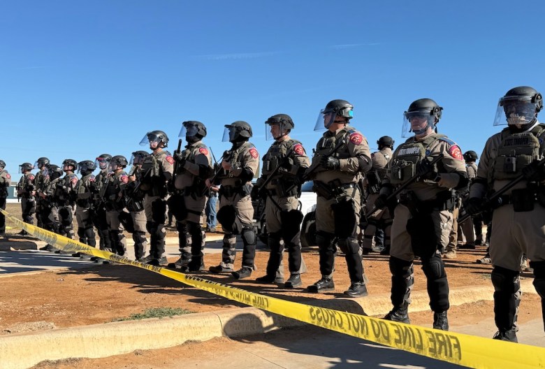 DPS troopers in riot gear form a line in front of protesters. 