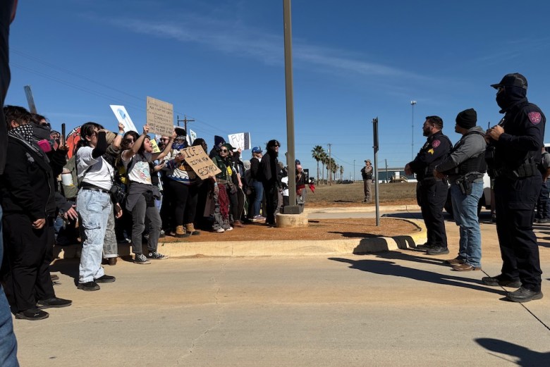 Law-enforcement personnel stand between protesters and the Dilley detention center.