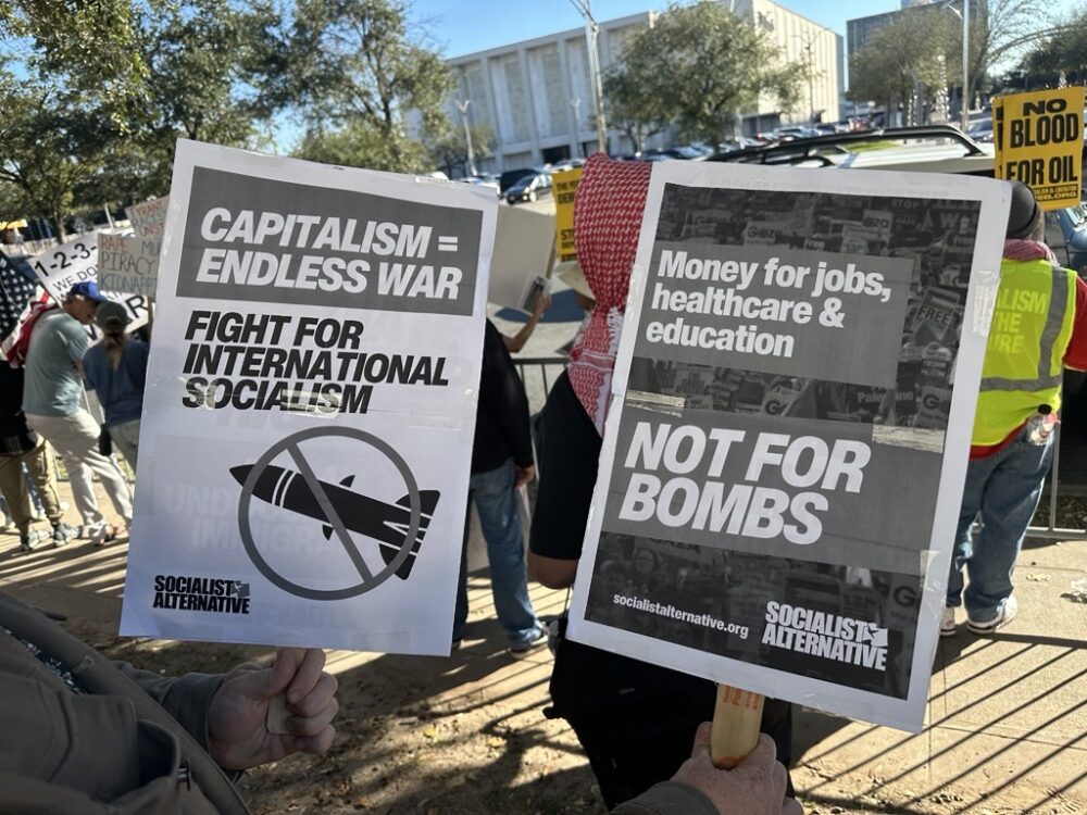 A Houston protester holds signs at a demonstration against U.S. intervention in Venezuela on Sunday, Jan. 4, 2026.