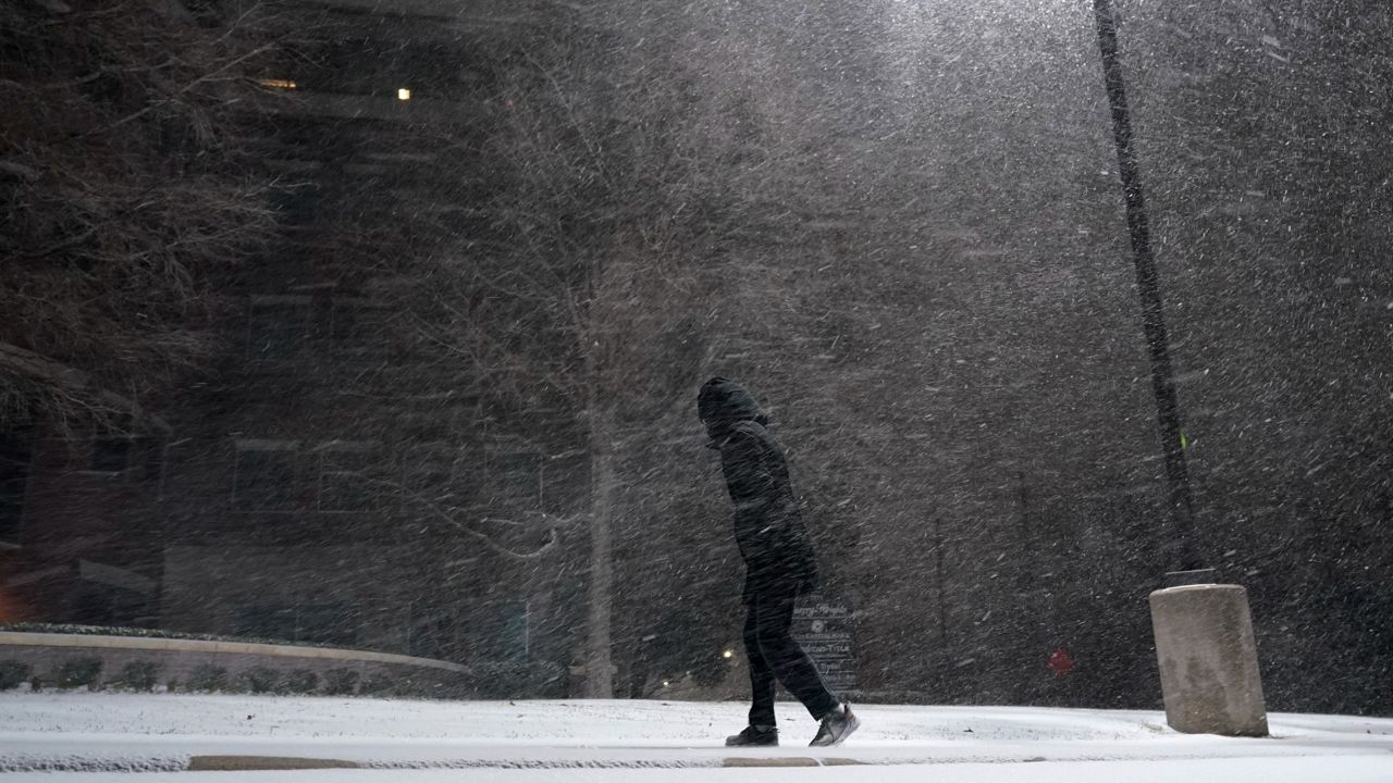 In this Feb. 14, 2021, file photo, woman walks through falling snow in San Antonio. As temperatures plunged and snow and ice whipped the state, much of Texas' power grid collapsed, followed by its water systems. Tens of millions huddled in frigid homes that slowly grew colder or fled for safety. (AP Photo/Eric Gay)