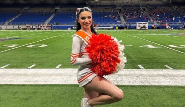Brianna Aguilera with pom poms in a cheerleading uniform on a football field