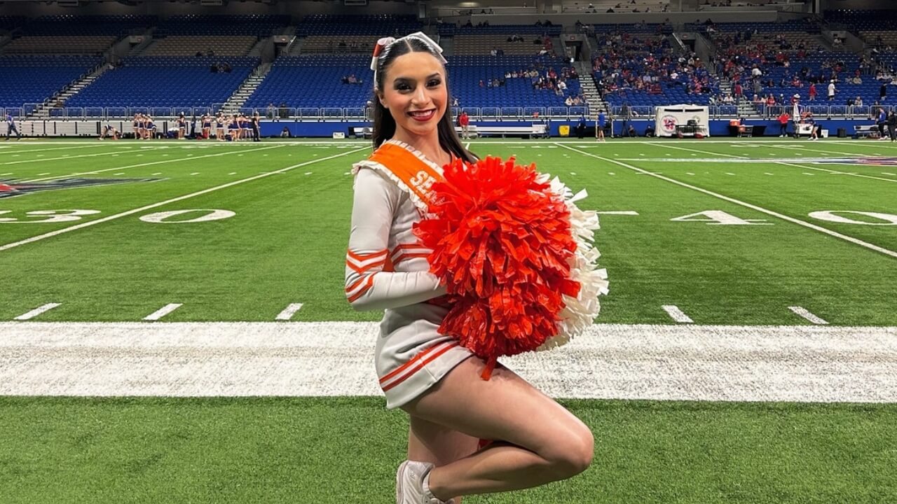 Brianna Aguilera with pom poms in a cheerleading uniform on a football field