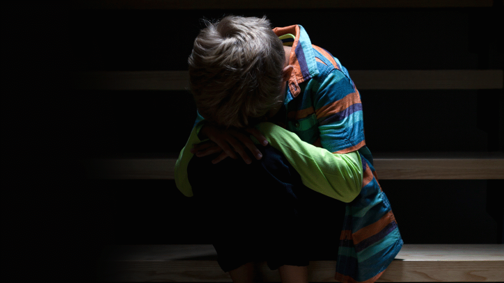 A photo illustration of a scared child sitting by themselves.
