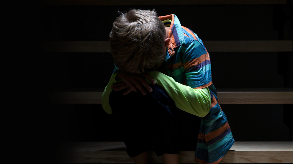 A photo illustration of a scared child sitting by themselves.