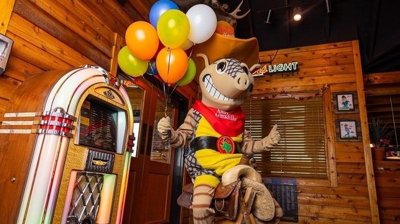 Mascot Andy Armadillo sitting on the birthday saddle with a bunch of balloons
