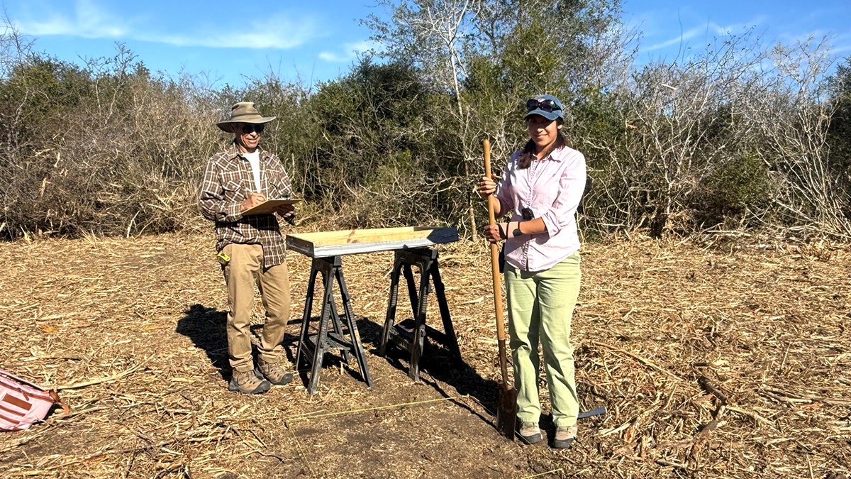 Student smiling and holding stick at archaeological site