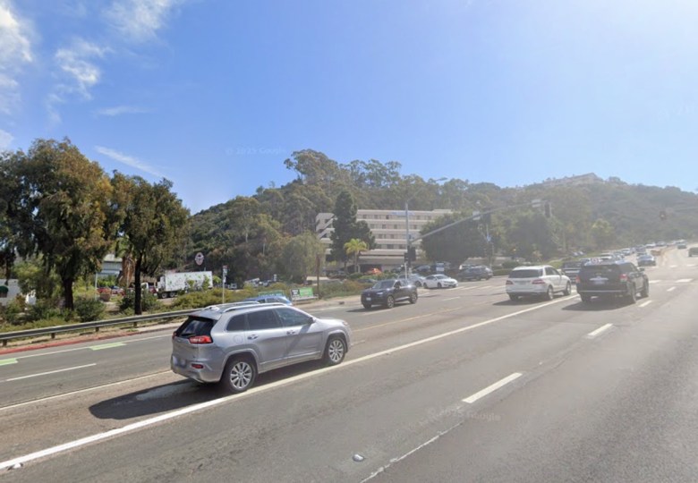A wide roadway is shown, with several cars moving in both directions, on a backdrop of a bright blue sky.