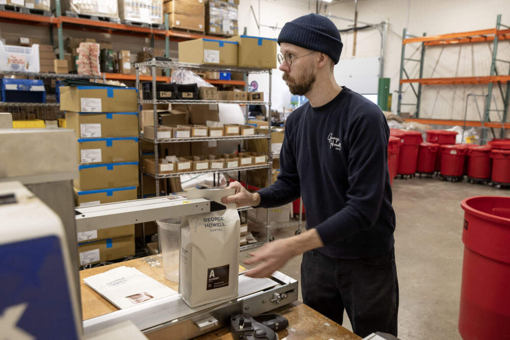 Kyle Miller feeds a bag of just roasted coffee into a bagging machine in the production area at the George Howell Coffee roastery in Acton, Mass. (Robin Lubbock/WBUR)