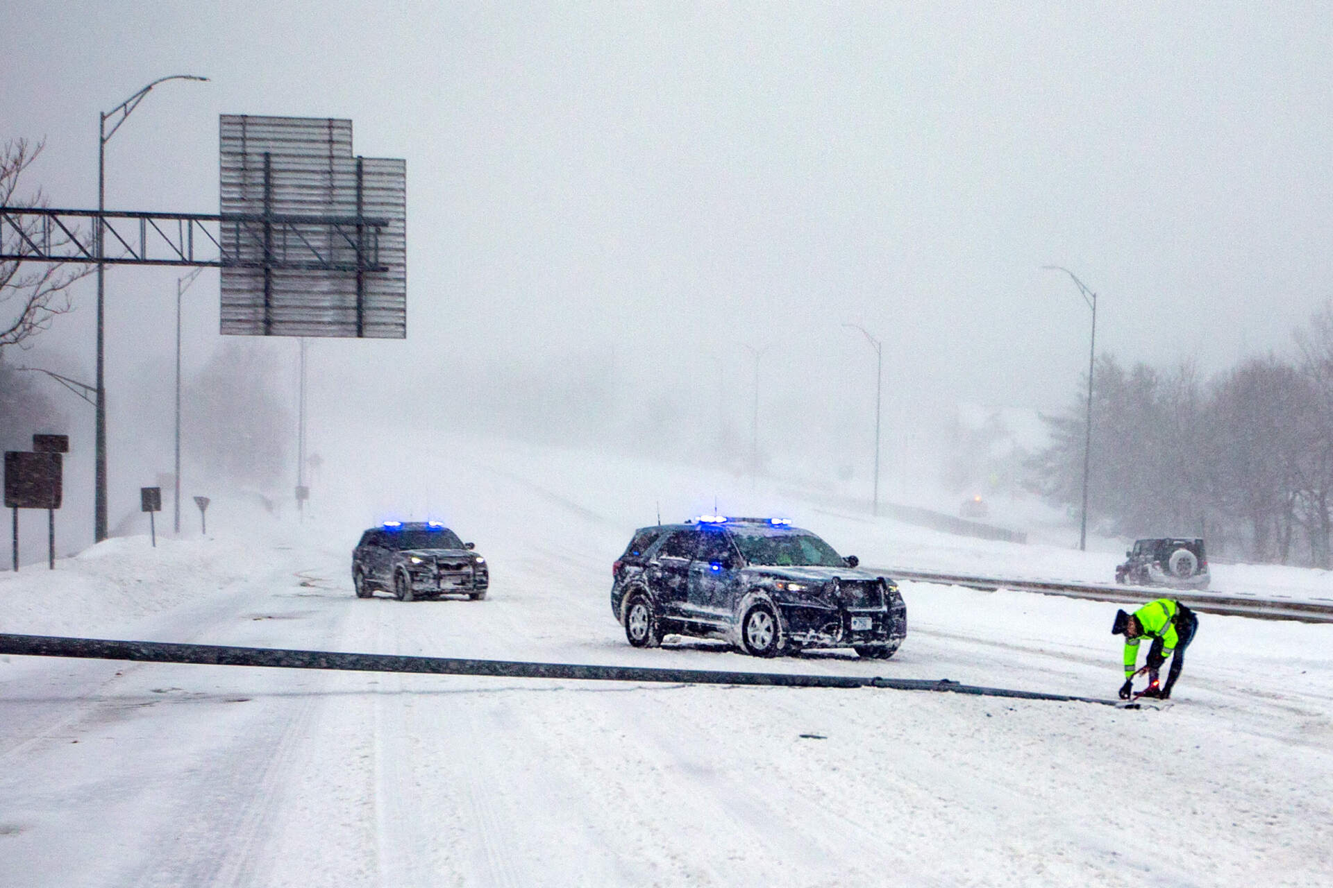 A Massachusetts State Police officer lays down flares to mark a light post straddling two lanes blown down by the winds of the nor’easter on Rt. 2 in Belmont, Feb. 23, 2026. (Jesse Costa/WBUR)