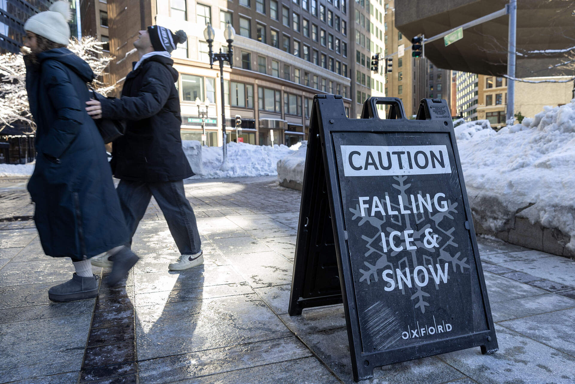 Pedestrians walk past a sign warning of falling ice and snow in downtown Boston after the storm. (Robin Lubbock/WBUR)