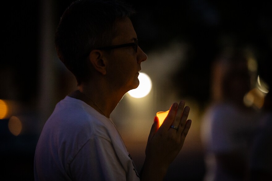 A woman in a white shirt holds a candle in the darkness.