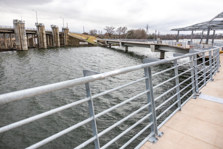 A view of the Longhorn Dam from the new wishbone bridge. A steel railing runs alongside of the bridge.