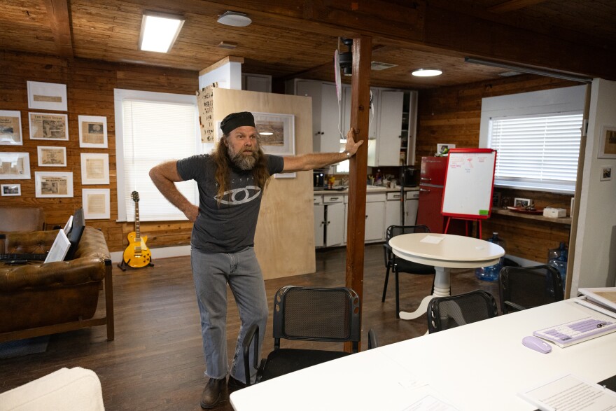 A man puts his arm out as he leans against a pole in an office. 