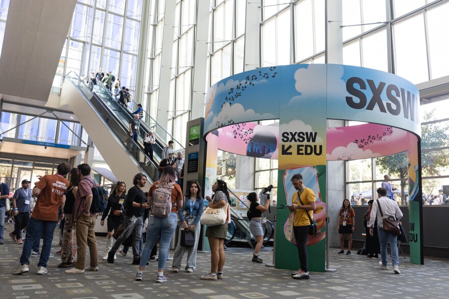 A crowd is shown inside a building with an escalator and tall windows. There is SXSW signage to the right side. 