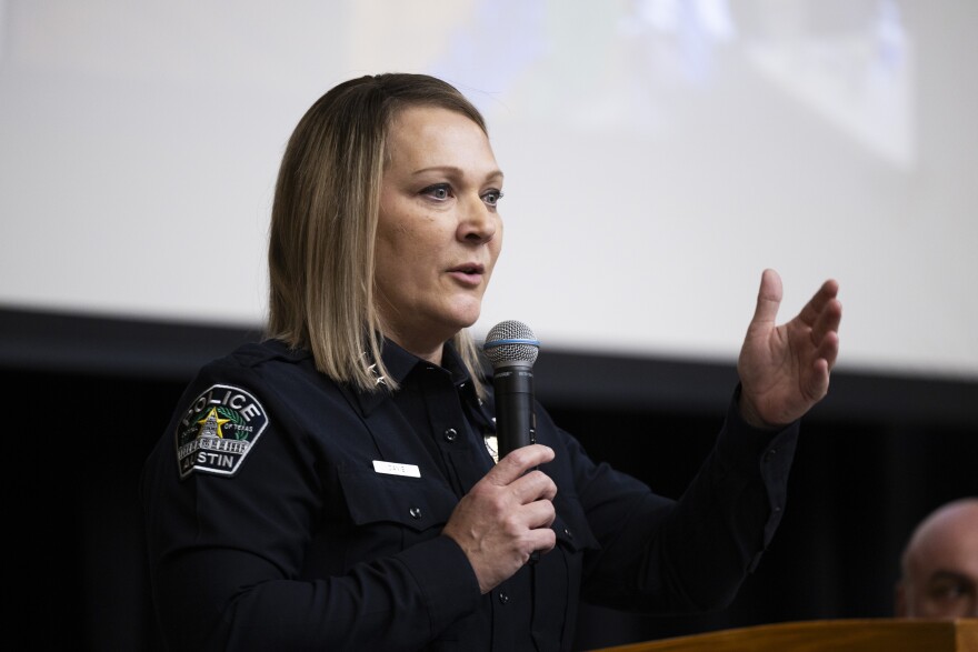 A woman in a police uniform gestures as she speaks into a microphone. 