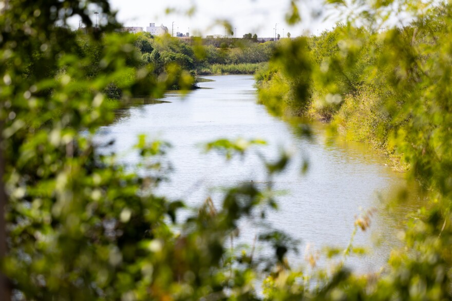 A river is shown beyond trees in the foreground.