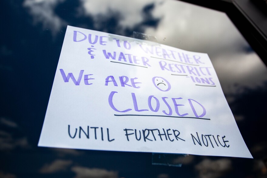 A handmade sign on a storefront door declaring closure due to lack of water and bad weather.