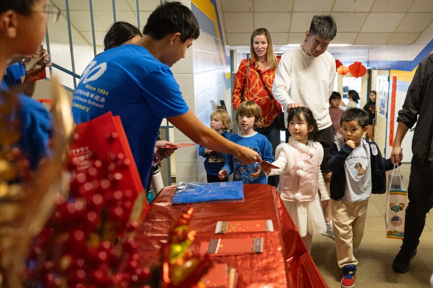 A man standing at a table that has red items on it hands a red envelope to a small child.