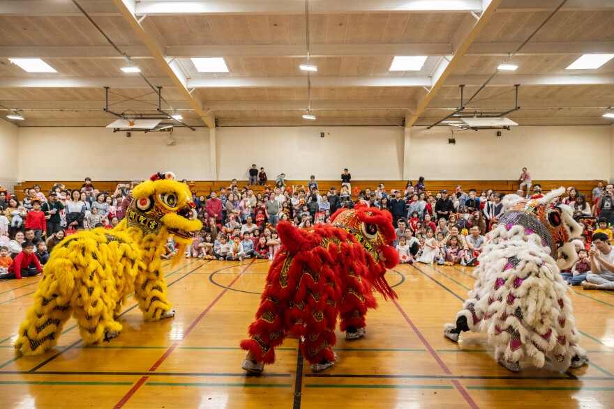 People in the background watch three dragons dancing,with people moving them from underneath, as part of a lunar new year event.