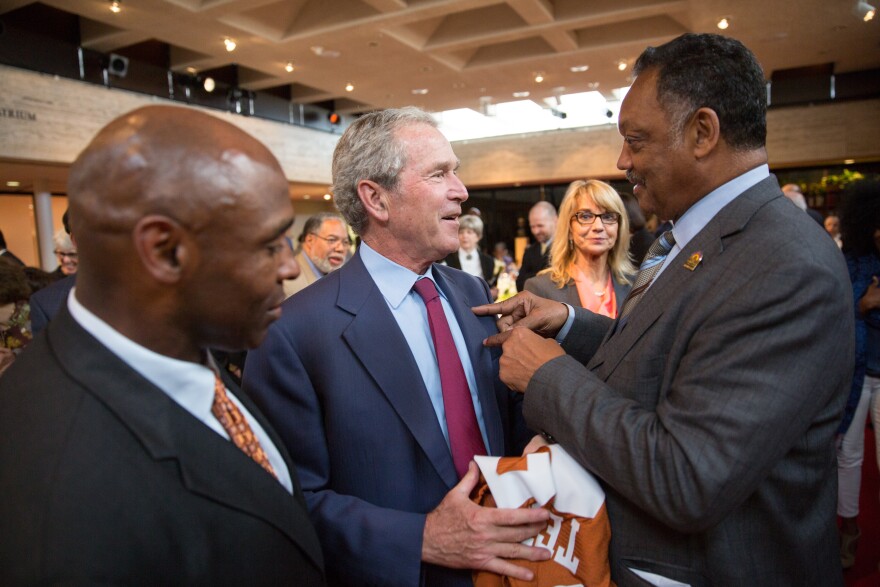 The men speak in a crowded room, the man on the right points to the man in the middle 