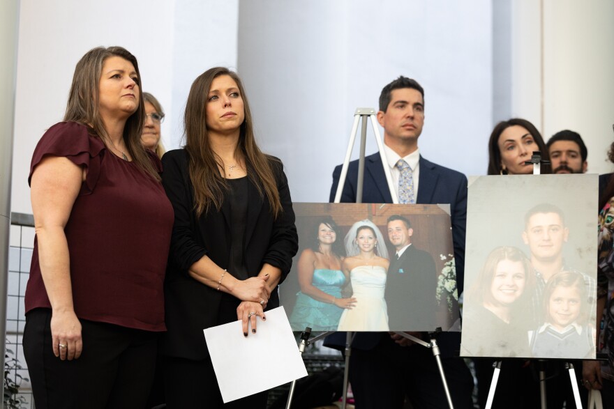 Two women stand next to enlarged family photos at a press conference. 