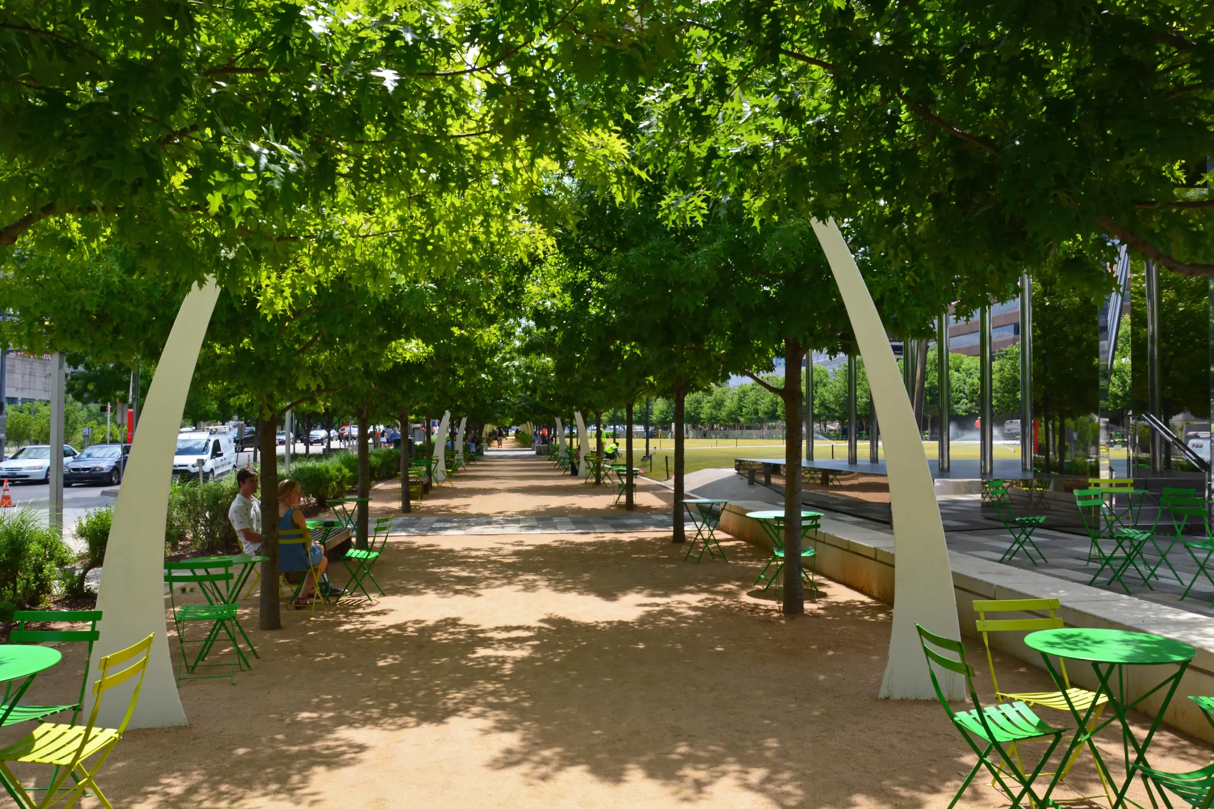 Public seating under oak trees and decorative arches lining the promenade at Klyde Warren Park in downtown Dallas.