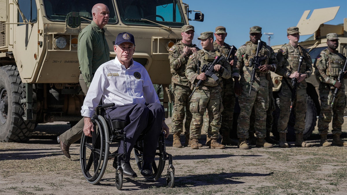 Gov. Abbott at the border with the National Guard standing behind him.