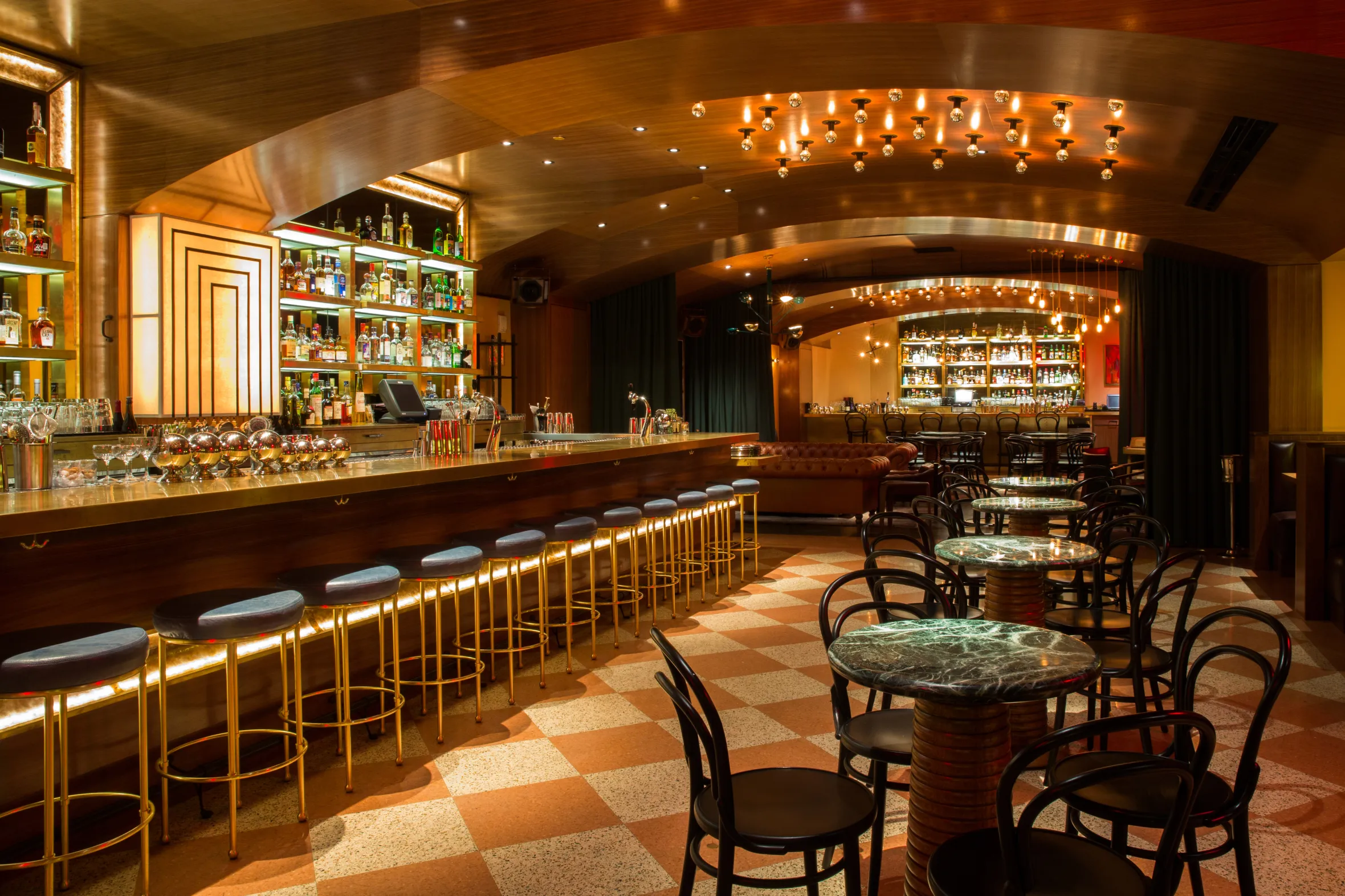 The interior of the Midnight Rambler bar at The Joule Hotel, showing a long bar with stools, tables, and a lounge area.