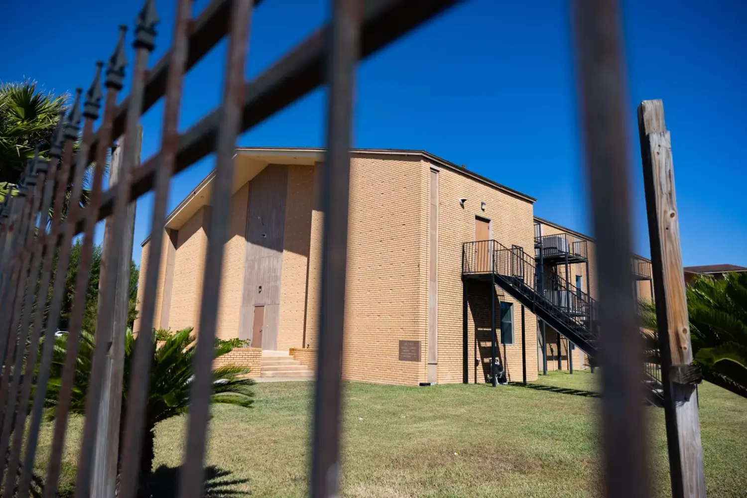 A building is seen in the background through a metal fence.