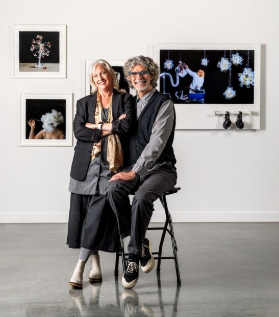 Artist duo Hillerbrand + Magsamen with their artworks on a wall behind him.