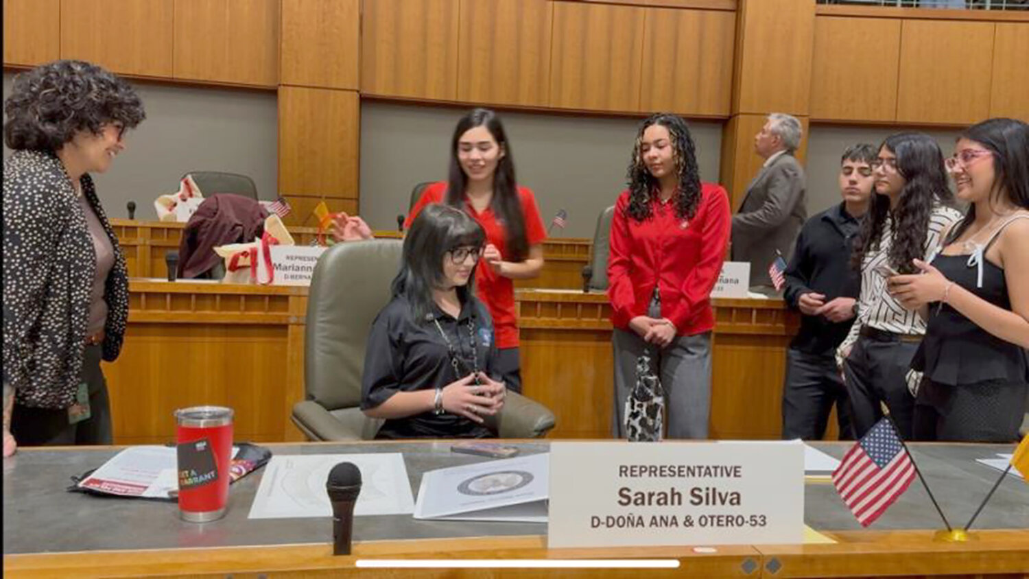 Representative Sarah Silvia (D-Do&ntilde;a Ana & Otero) visits with students from Gadsden Independent School District while Emily Smolik, a sophomore at Chaparral High School, sits in her seat on the House floor.
